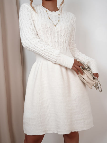 Robe pull torsadée beige portée par une mannequin blonde avec un sac à main